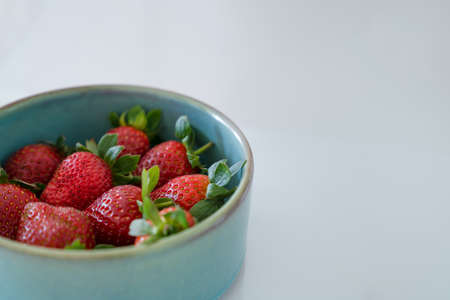 Red fresh strawberries with green leaves in plate on gray background. Side view, copy spaceの写真素材
