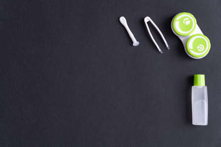 Container with contact lenses, tweezers, suction cup and bottle with solution on a black background,...
