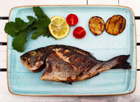 Fried fish with vegetables and herbs lies on light blue plate - tray, top view, close-up. Restaurant...