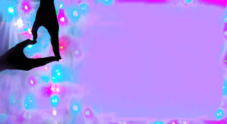Hands are folded in form of heart on background of unfocused multicolored lights and pink...