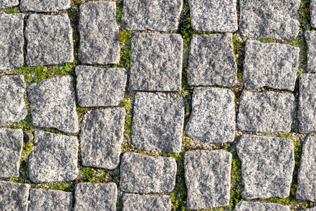 Stone road paved with asymmetrical stones with sprouted grass at seams. Textured background, top viewの写真素材