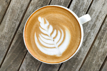 White cup of coffee with pattern on top of foam, against background of wooden table, top viewの写真素材