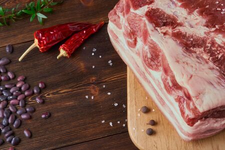 Raw pork belly and red beans on the light cutting board and dark wooden brushedの写真素材