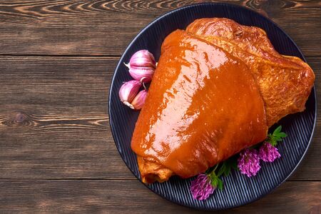 Smoked pork knuckle, garlic and clover flowers. Black corrugated plate and rustic woodenの写真素材