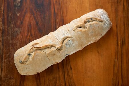 Ciabatta with olives on an old scratched mahogany table. Fresh Italian homemade wheat bread.の写真素材
