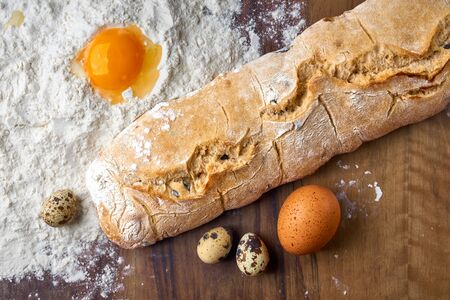 Homemade olive ciabatta, farm quail and chicken eggs on a wooden tabletop. Fresh natural diet healthy food. The process of making dough from flour and a broken egg is shown.の写真素材