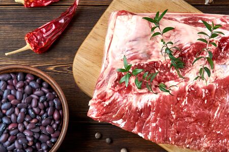 Raw pork belly and red beans on the light cutting board and dark wooden brushed background. Spices: peppercorns, hot peppers, salt. Rustic style image.の写真素材
