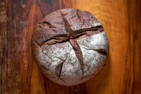 Round rye bread with molasses on the old scratched mahogany table. Home baked bread.の写真素材