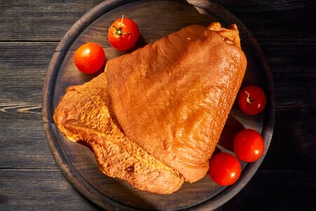 Smoked pork knuckle with fresh cherry tomatoes, illuminated by the slanting gold rays of the sun. Rustic cutting board and wooden background.の写真素材