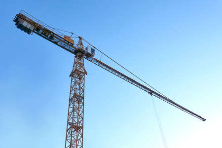 Tall construction crane against the blue sky. Tower crane for lifting loads in the construction of...