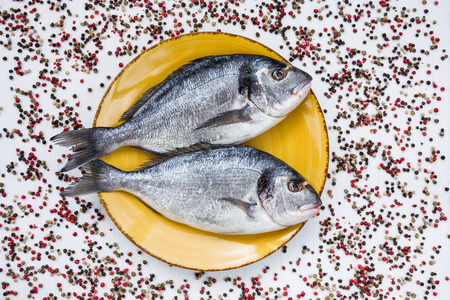 Raw dorado fish on yellow plate with peppercorns on white table. Top view, copy spaceの写真素材