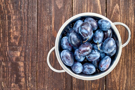 Blue plums in rustic colander on old wooden table. Organic food. Copy space, top viewの写真素材