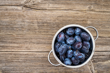 Fresh blue plums in rustic colander on old wooden table. Organic food. Top view, copy space.の写真素材