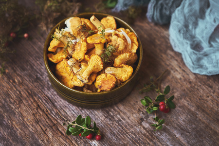 Raw wild mushrooms chanterelles in bowl on old wooden background. Cantharellus cibarius - edible mushroom. English: chanterelle, golden chanterelle, girolle.の写真素材
