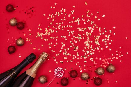Two Champagne bottles with Christmas decorations and candy on red background. Flat lay of christmas, anniversary, new year celebration conceptの写真素材