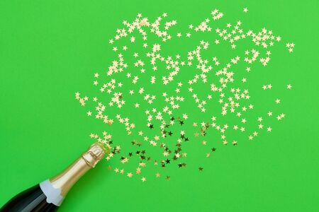 Champagne bottle with confetti stars on green background. Flat lay of christmas, anniversary, new year celebration concept. Copy space, top view. Color of the Year 2019.の写真素材