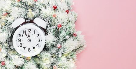 Christmas background. White Christmas wreath with decoration and alarm clock on pink background....