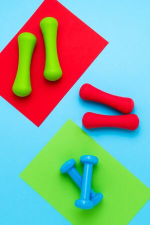 Red, blue and green dumbbells lie on colorful background. The concept of healthy lifestyle. Copy space for text, top viewの写真素材
