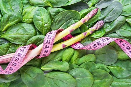 Green vegetables background. Green spinach leaves and asparagus with tape measure. Healthy food and...