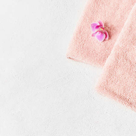 Rolled pink towel and pink orchid flower on white concrete background. Minimalist scandinavian style. SPA conceptの写真素材