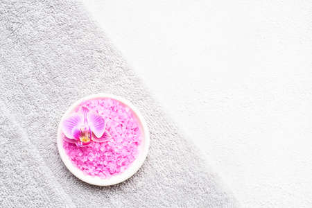 Rolled grey towels, pink bath salt and orchid flower on a white concrete background. SPA concept....