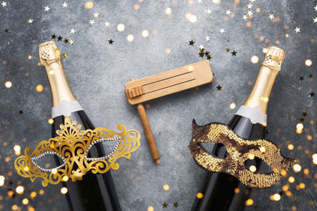 Two champagne bottles, golden carnival masks. noisemaker and confetti stars on a grey background. Carnival backgroundの写真素材