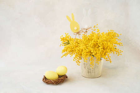 Earter eggs and Mimosa flowers bouquet in a vase on light background. Easter concept, copy spaceの写真素材
