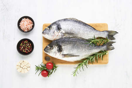 Raw dorado fish with spices on a wooden cutting board on a white background. Mediterranean seafood...