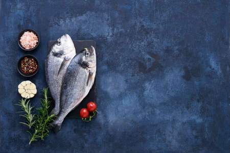 Raw dorado fish with spices on a slate cutting board on a blue background. Mediterranean seafood...