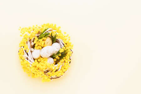 Decorative Easter eggs and mimosa wreath on a beige background. Easter background. Top view, copy space for textの写真素材