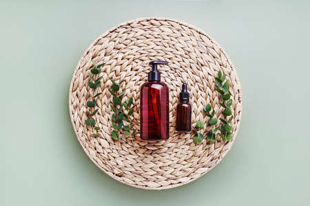 Dropper bottle of essential oil or serum, eucalyptus and dark dispenser bottle of shower gel, on...