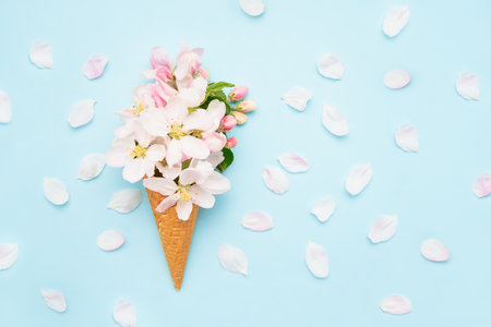 Waffle ice cream cone with apple blossom flowers on a light blue background. Spring concept. Copy...