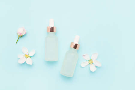 Two glass dropper bottles for cosmetic use and apple tree blossom flowers on a light blue...