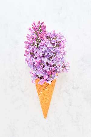 Waffle ice cream cone with pink lilac blossom flowers on a white marble background. Spring conceptの写真素材