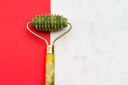 Green jade face roller on a red-white background. SPA concept. Top view, copy space for textの写真素材