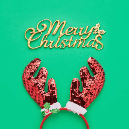 Christmas background. Text Merry Christmas and toy deer antlers on a green backdrop. Flat layの写真素材