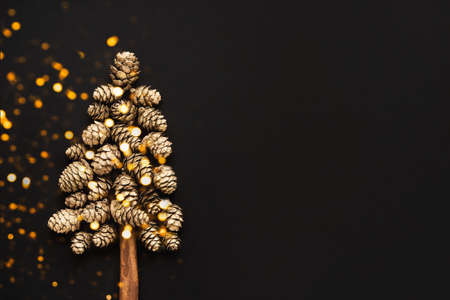 New Year and Christmas card. Christmas tree made from golden cones on a black background. Minimal...