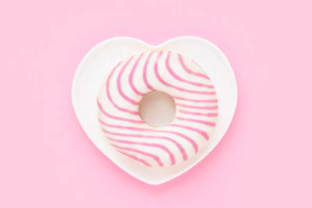 Striped pink donut in heart shape plate. Valentines day concept. Top view, copy space for text.
