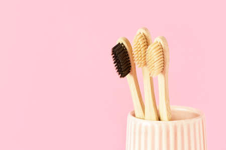 Natural bamboo toothbrushes in a ceramic glass on pink background. Eco-friendly, zero-waste concept