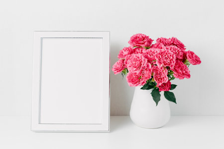 White frame mockup and pink roses bouquet in a white vase. Copy space for textの写真素材