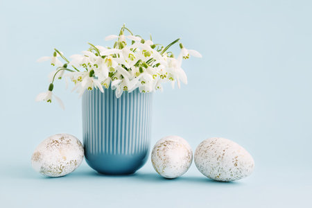 Easter greeting card with snowdrops in a vase and Easter eggs on a light blue background. Copy spaceの写真素材