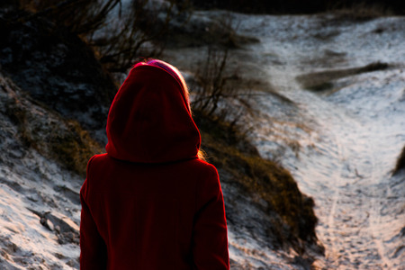 Relaxing while watching the sunset. Shot of a girl in a red coat at the seaside.