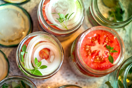 Canning fresh tomatoes with onions for winter in jelly marinade. A shot of basil leaves on top of a...