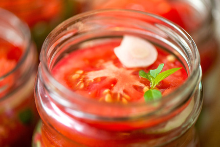 Canning fresh tomatoes with onions for winter in jelly marinade. A shot of basil leaves on top of a red ripe tomato slices and onion rings being put in jar. Vegetable salads for winter.の写真素材