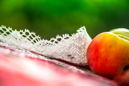 Golden autumn. Macro shot of crochet white linen lace trim, natural linen tablecloth with rose print, red, yellow apples on table on green background. Time for dinner. Perfect time for picnic outsideの写真素材