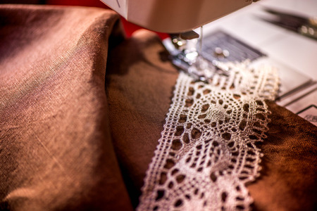 A macro shot of a crochet natural linen lace trim and dark brown linen fabric,being used while sewing a linen tablecloth by using a sewing machine and needles. Making table decorations, flax linenの写真素材