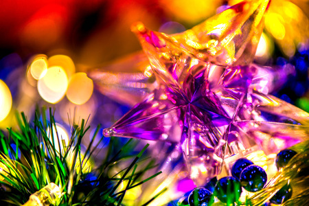 Abstract, blurry, vibrant and colorful background. Macro shot of a blue, purple and green Christmas decorations and a Christmas star on a lit Christmas Treeの写真素材