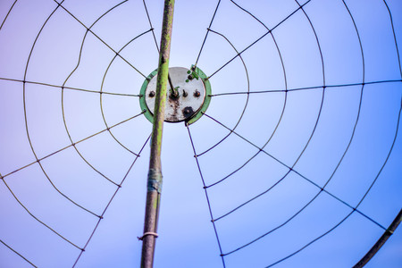 Old, corroded, round, metal television, radio antenna with grid, screws, bolts on clear blue sky background. Antenna receiving, transmitting, capturing signals from satellites in different locationsの写真素材