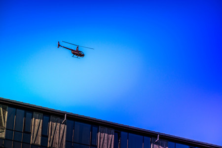 Military helicopter flying in the sky over a city and crowded event, taking photos, filming from...