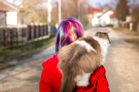 A scene of best friends. Acat is sitting on a shoulder of a girl with colorfully dyed hair. Taking cat a for a walk. Blue and pink hair. Lovely, fluffy, cute kitten, maine coon cat. Sunny spring day.の写真素材